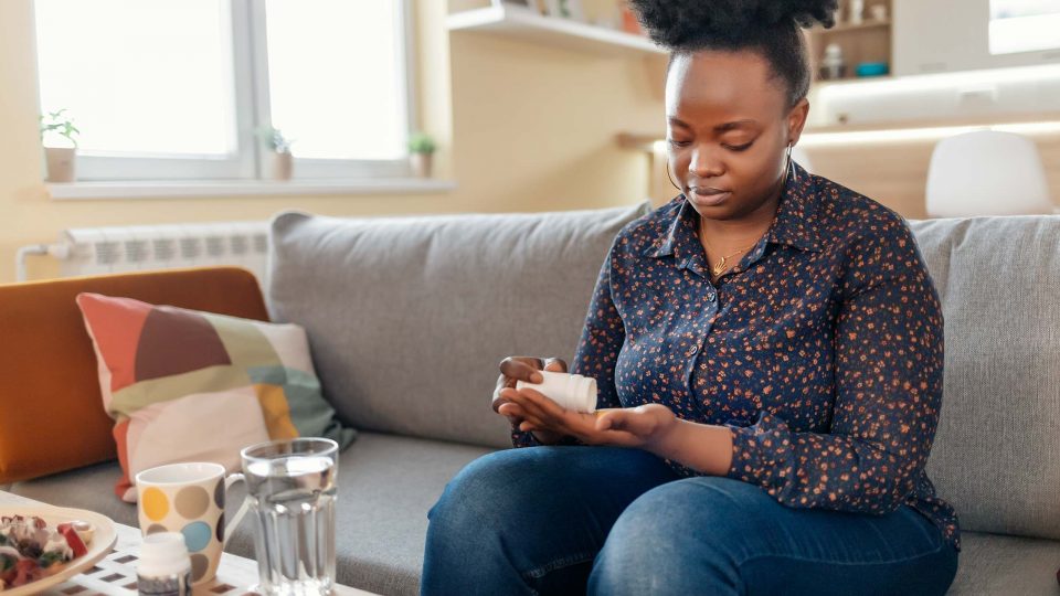 Person Pouring Out Pill from Bottle into Hand While Sitting on Couch at Home