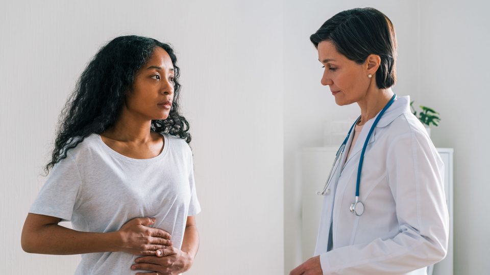 Patient Sitting in Exam Room and Clutching Stomach as Doctor Performs Assessment