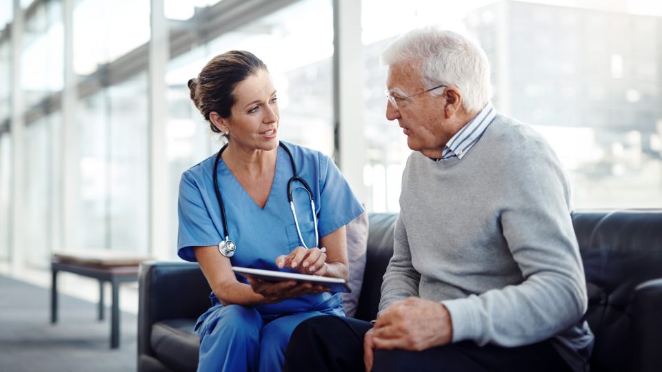 Doctor seated with patient on couch, discussing health record information on a tablet