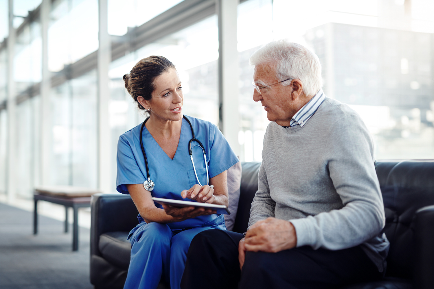 Doctor seated with patient on couch, discussing health record information on a tablet