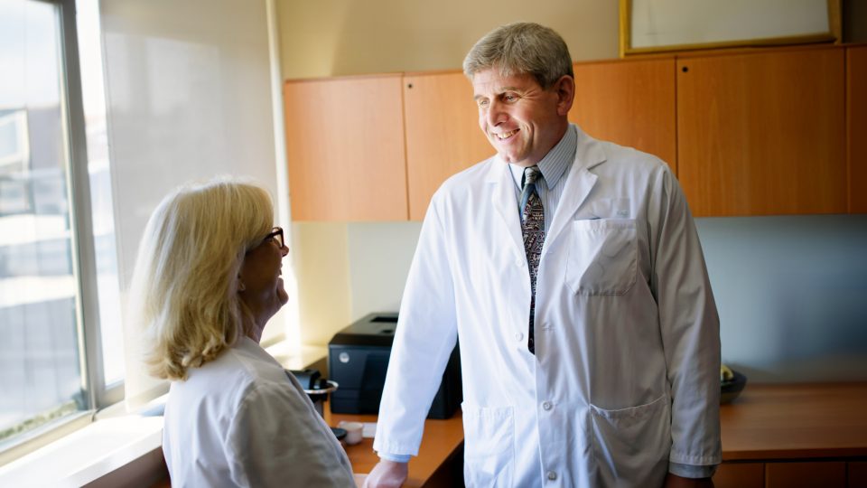 Dr. Joshua Chodosh smiling and talking with colleague in office