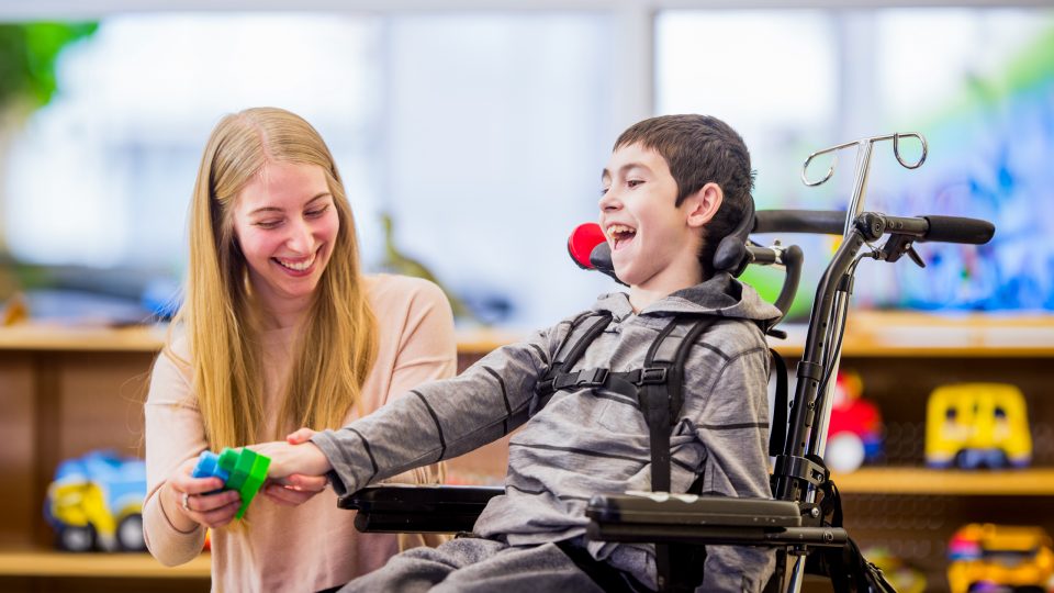 Smiling child in wheelchair playing with blocks with assistance from a caregiver